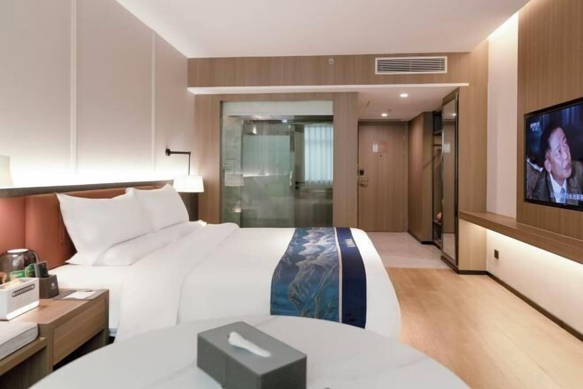 A hotel room with a bed, bedside table, TV, and a glass door leading to a bathroom.