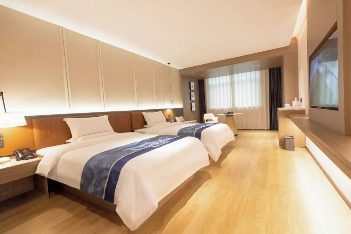 A hotel room with two beds, a TV, a desk, and a window with curtains.