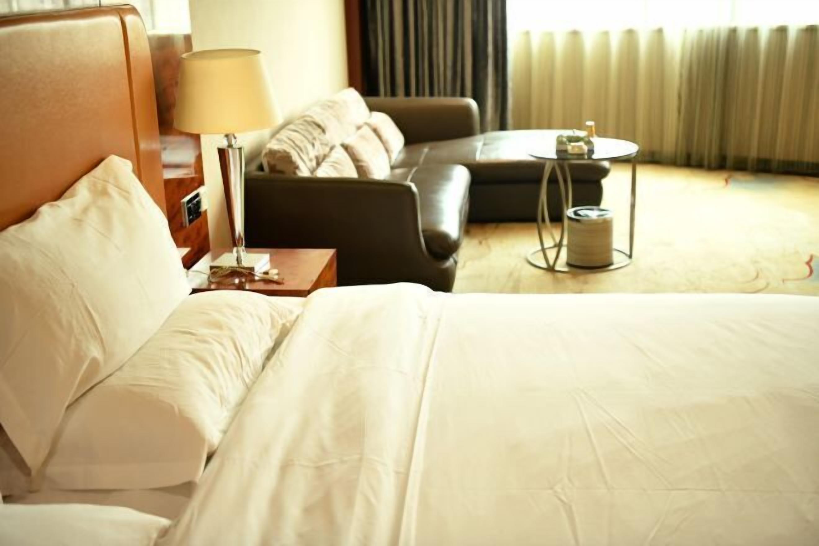 Una habitación de hotel con cama, escritorio con lámpara, sofá y una mesita redonda.