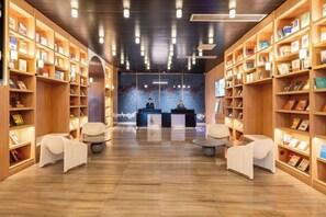 A hotel lobby with wooden bookshelves, seating areas, and a reception desk.