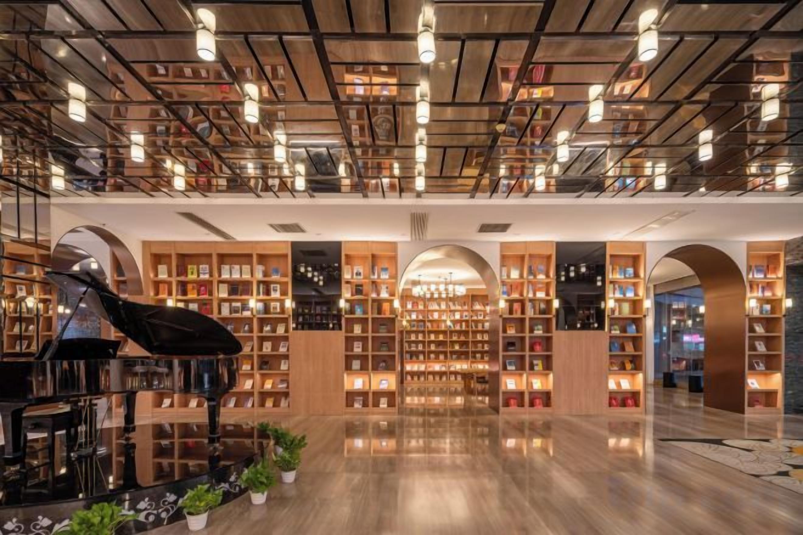 A spacious library with bookshelves, a grand piano, and a polished wooden floor.
