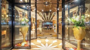 Un'hall dell'hotel con una scalinata centrale, porte in vetro e ampi vasi decorativi.