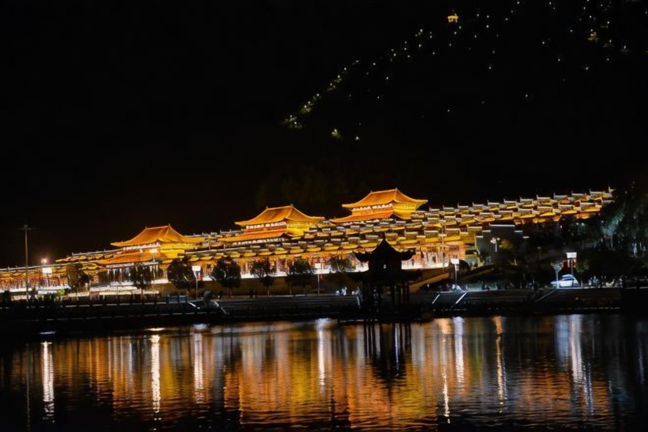 A traditional building with multiple roofs, illuminated at night, reflecting on a body of water.
