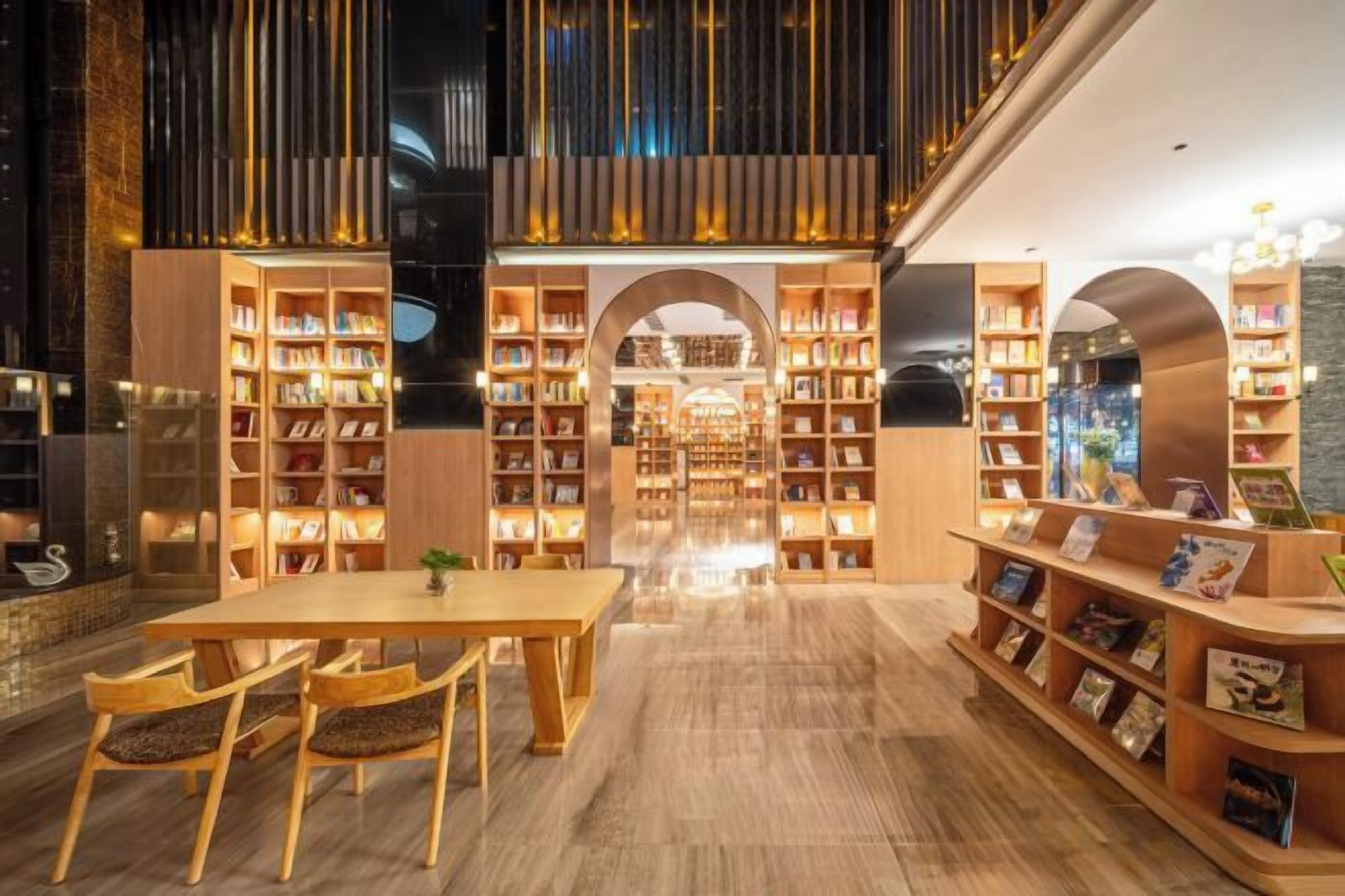 L’intérieur d’une bibliothèque moderne, avec des étagères en bois, une table centrale et des sièges.