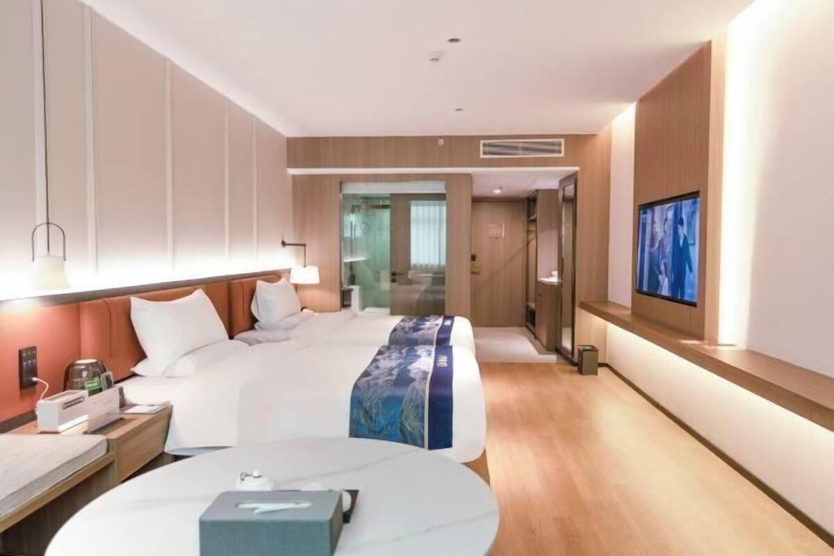 A modern hotel room with a large bed, bedside tables, a TV, and a view of the hallway.