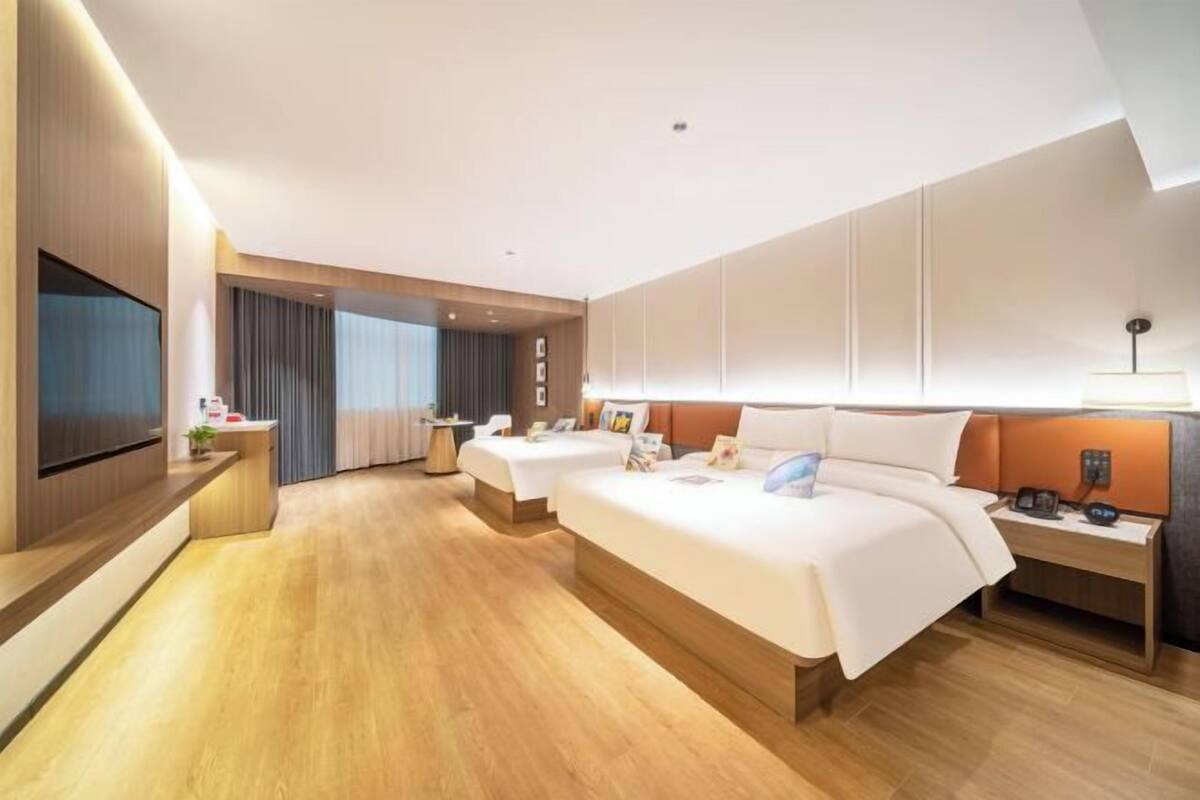 A hotel room with a large bed, bedside tables, a TV, and a desk with a lamp.