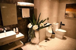 Un baño moderno con un lavabo de mármol, inodoro y un florero con flores blancas.