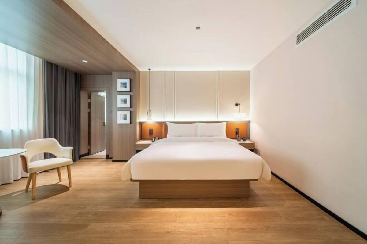A modern hotel room with a large bed, bedside lamps, a small table, and a chair.