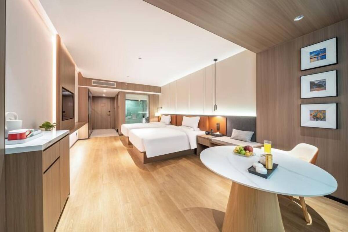 A modern hotel room with a large bed, a dining table, a kitchen area, and a bathroom.