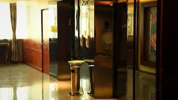 A hotel corridor with a polished floor, a reception desk, and a glass door with a number sign.