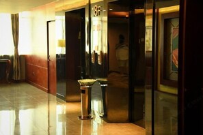 A hotel corridor with a polished floor, a reception desk, and a glass door with a number sign. - NEW BAO HUI · HAPPY SLEEP HOTEL (Ganzhou)