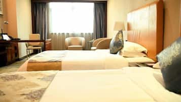 A hotel room with a large bed, two armchairs, a desk, and a window with curtains.