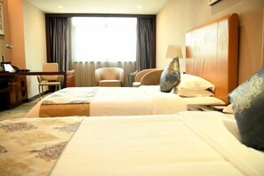 Een hotelkamer met een groot bed, twee fauteuils, een bureau en een raam met gordijnen.