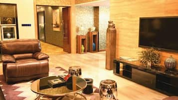 A modern living room with a leather sofa, a glass coffee table, and a flat-screen TV mounted on the wall.