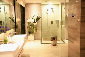 A modern bathroom with a glass shower enclosure, a white sink, and a vase of white flowers. - NEW BAO HUI · HAPPY SLEEP HOTEL (Ganzhou)