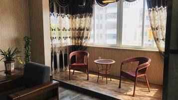 A room with a wooden floor, a sofa, two wicker chairs, a small table, and a window with patterned curtains.