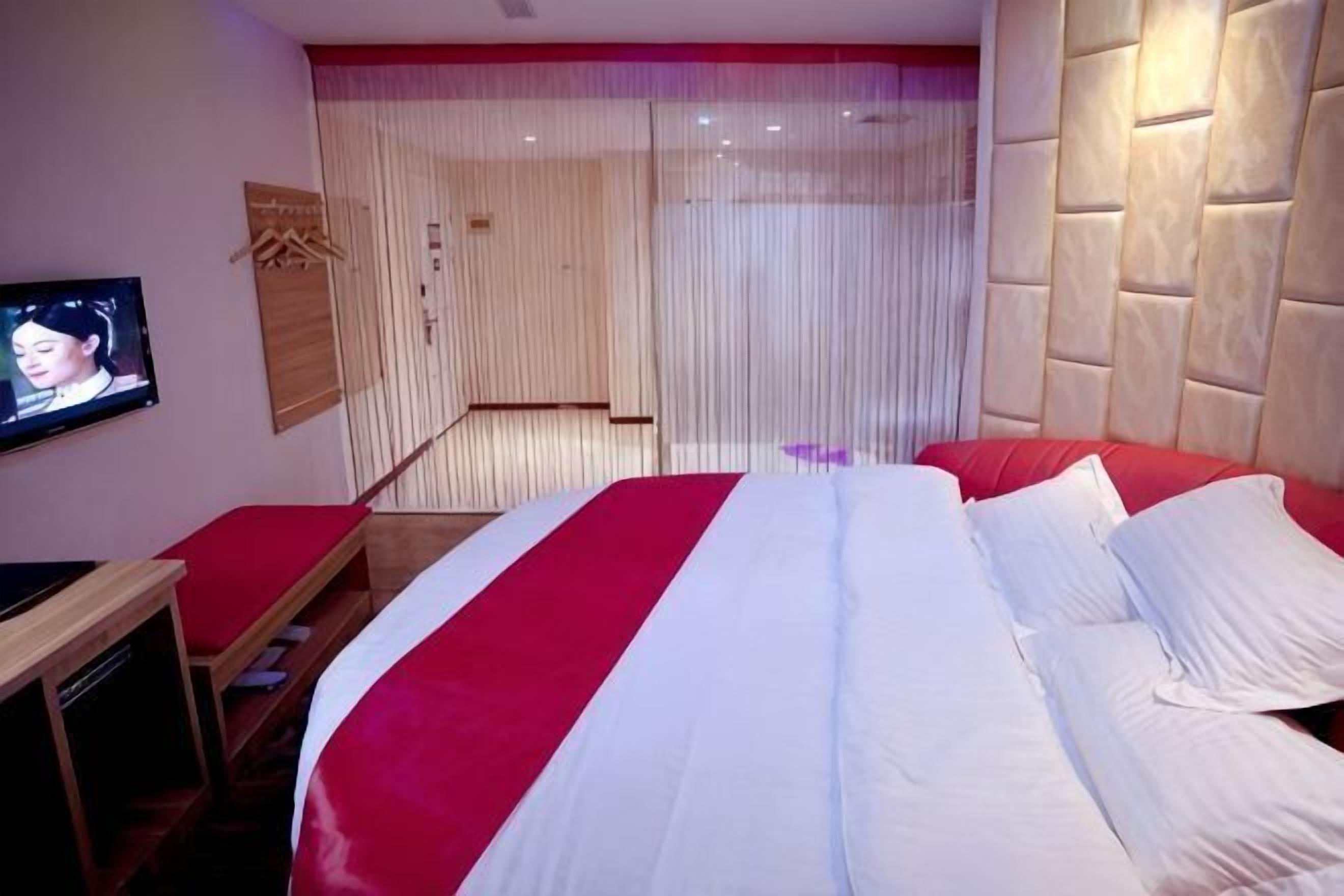 A hotel room with a large bed, a TV on the wall, and a wooden bench.