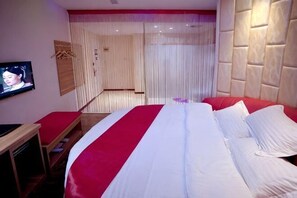 A hotel room with a large bed, a TV on the wall, and a wooden bench. - Huating Hotel (Jiangdu District Shaobo Ancient Town) (Yangzhou)