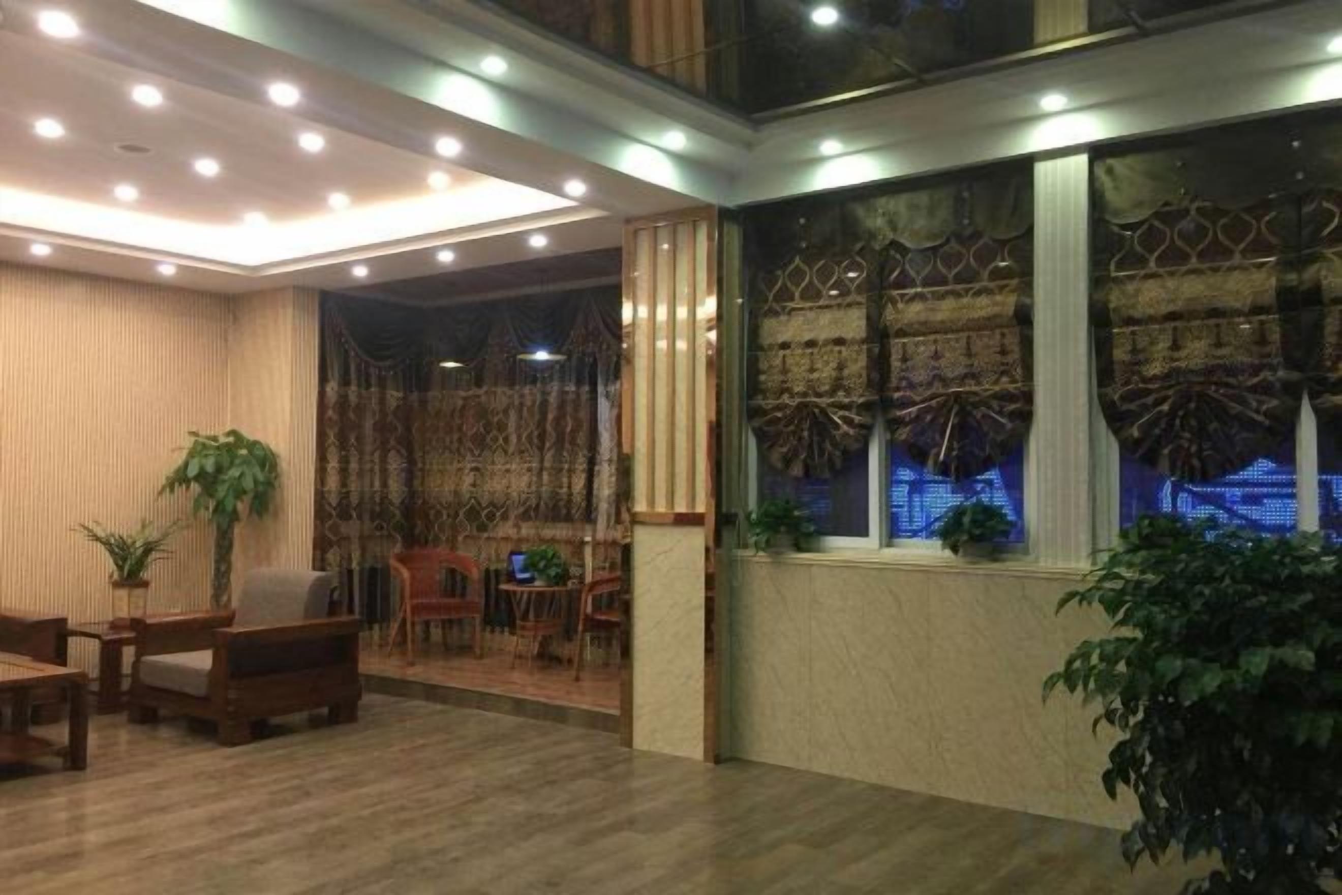 A hotel lobby with a wooden floor, seating area, and a large window with decorative curtains.