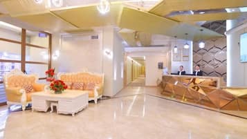 A hotel lobby with a reception desk, seating area, and a hallway leading to other rooms.