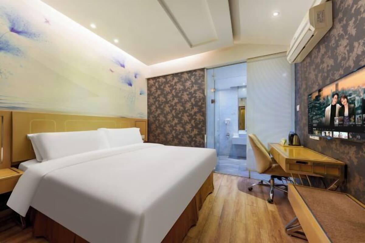 A hotel room with a large bed, a desk, and a wall-mounted TV.