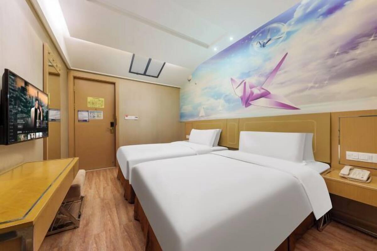 A hotel room with two beds, a desk, a TV, and a mural of a sailboat on the wall.