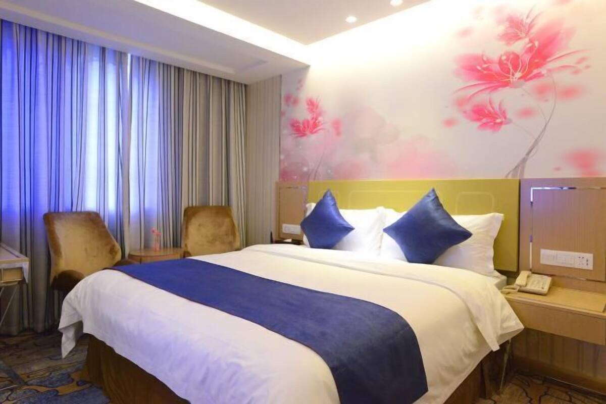 A hotel room with a large bed, two chairs, a desk, and a wall with floral artwork.