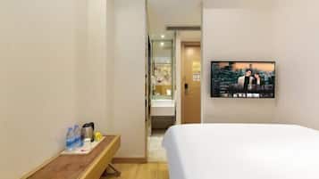 A hotel room with a bed, a TV mounted on the wall, a small table with a tray of items, and a bathroom visible through an open door.