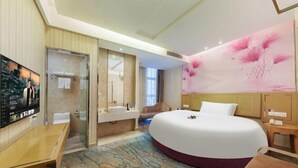 A hotel room with a large bed, a bathroom with a mirror, a TV, and a wall with a floral design. - Yongcui Hotel (Shenzhen Luohu Shuibei Jewelry City) (Shenzhen)