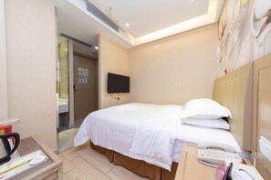 A hotel room with a bed, a desk with a telephone, a television mounted on the wall, and a door leading to another room.
