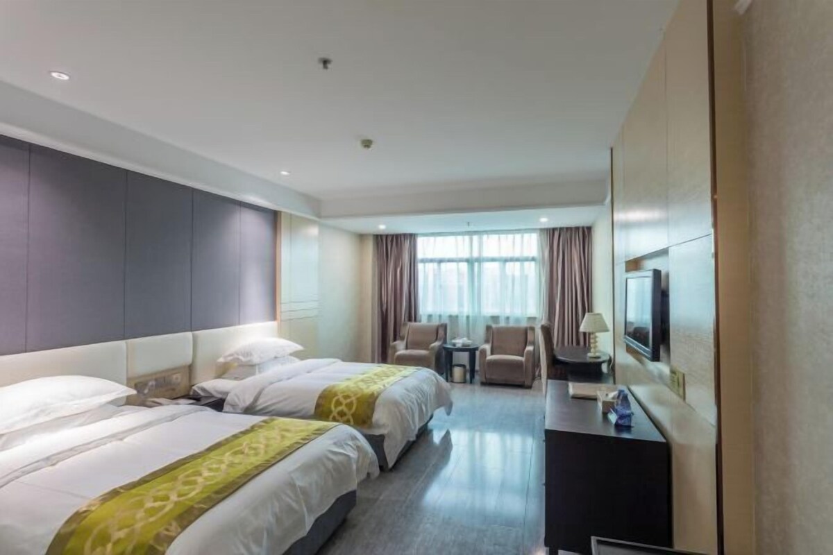 A hotel room with two beds, a desk, a chair, a TV, and a window with curtains.
