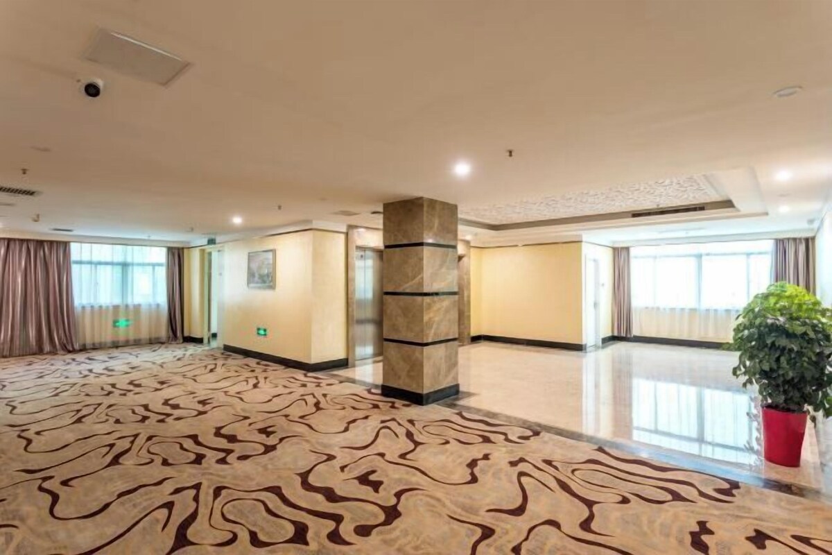 A spacious lobby with a patterned carpet, a central pillar, and a potted plant.