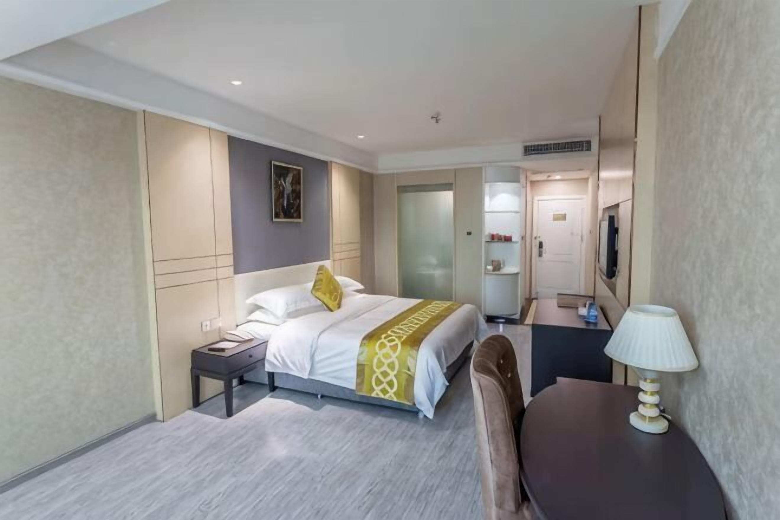 A hotel room with a bed, bedside table, lamp, and a desk with a chair.