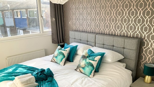 Una cama bien hecha con un cabecero gris, dos almohadas color turquesa y una manta turquesa.