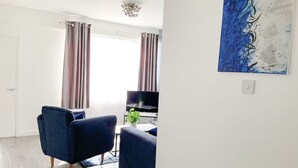 Una sala de estar con un sofá, un sillón, un televisor y un cuadro en la pared.