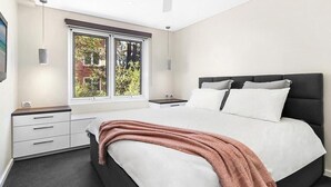 A modern bedroom with a bed, a nightstand, a dresser, a ceiling fan, and a window with a view of greenery. - Manly - Free parking, WIFI, Office, Pool, Coffee Machine (Manly)