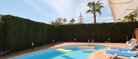 Piscina com espreguiçadeiras e uma palmeira ao fundo.