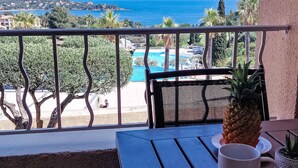 Een balkon met uitzicht op een zwembad, een ananas en een witte mok op een tafel.
