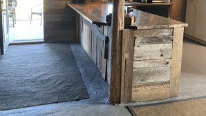 A rustic kitchen with wooden beams, a wooden island, a hanging light, and a view to the outside.