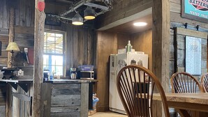 A rustic kitchen with wooden walls, a wooden dining table, and chairs. There is a refrigerator, a microwave, and a coffee maker on the counter.