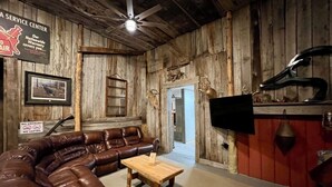 A rustic interior with a leather couch, a wooden coffee table, a television mounted on a wall, and a service center sign.