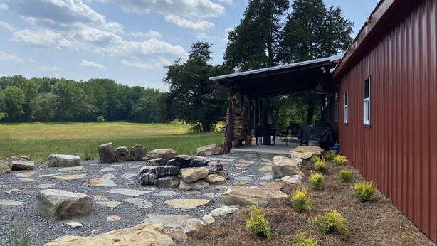A rustic cabin with a stone fire pit, surrounded by a gravel path and small plants.