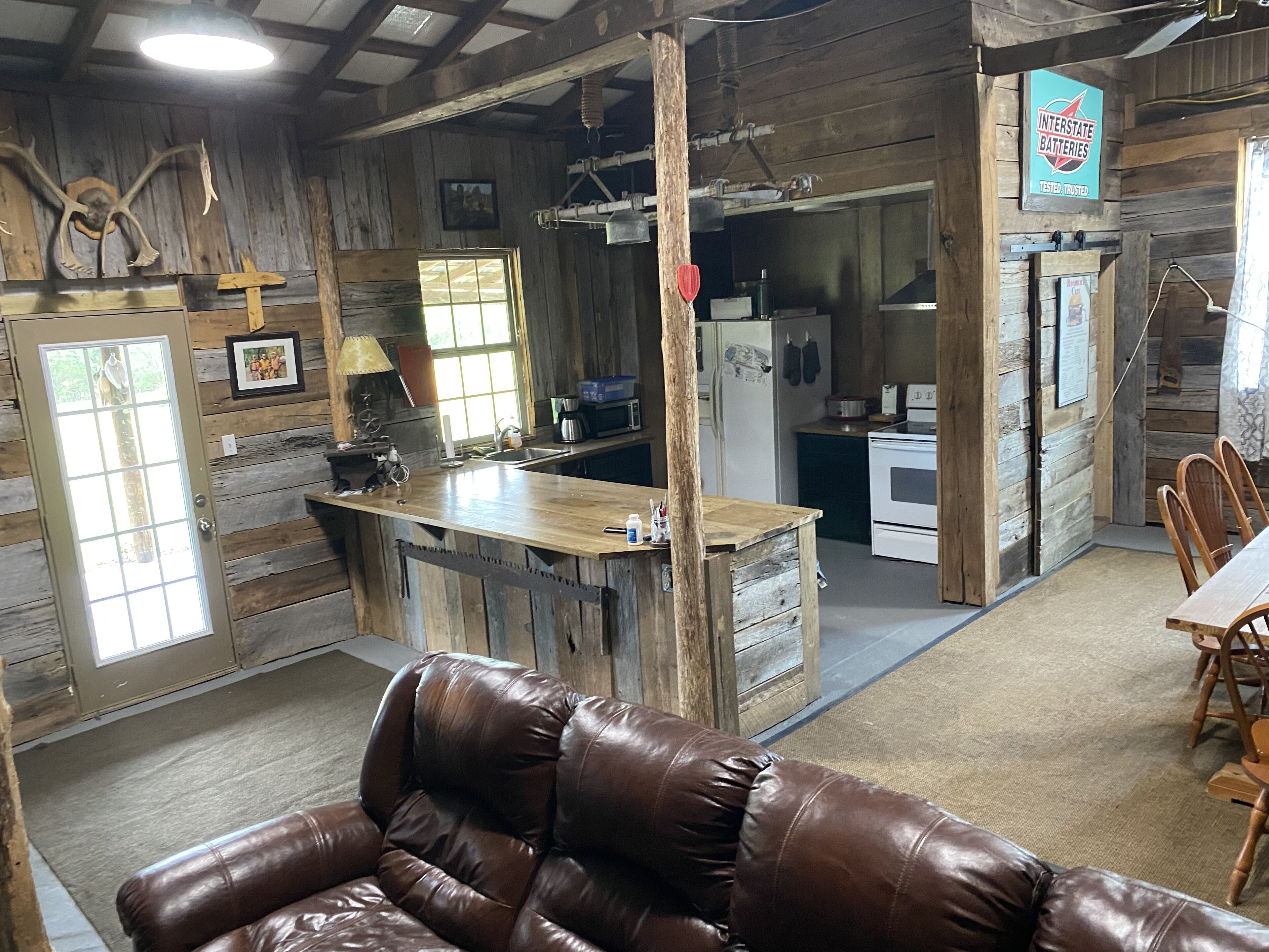 A rustic cabin interior with a wooden bar, a leather couch, a dining table, and a kitchen area.