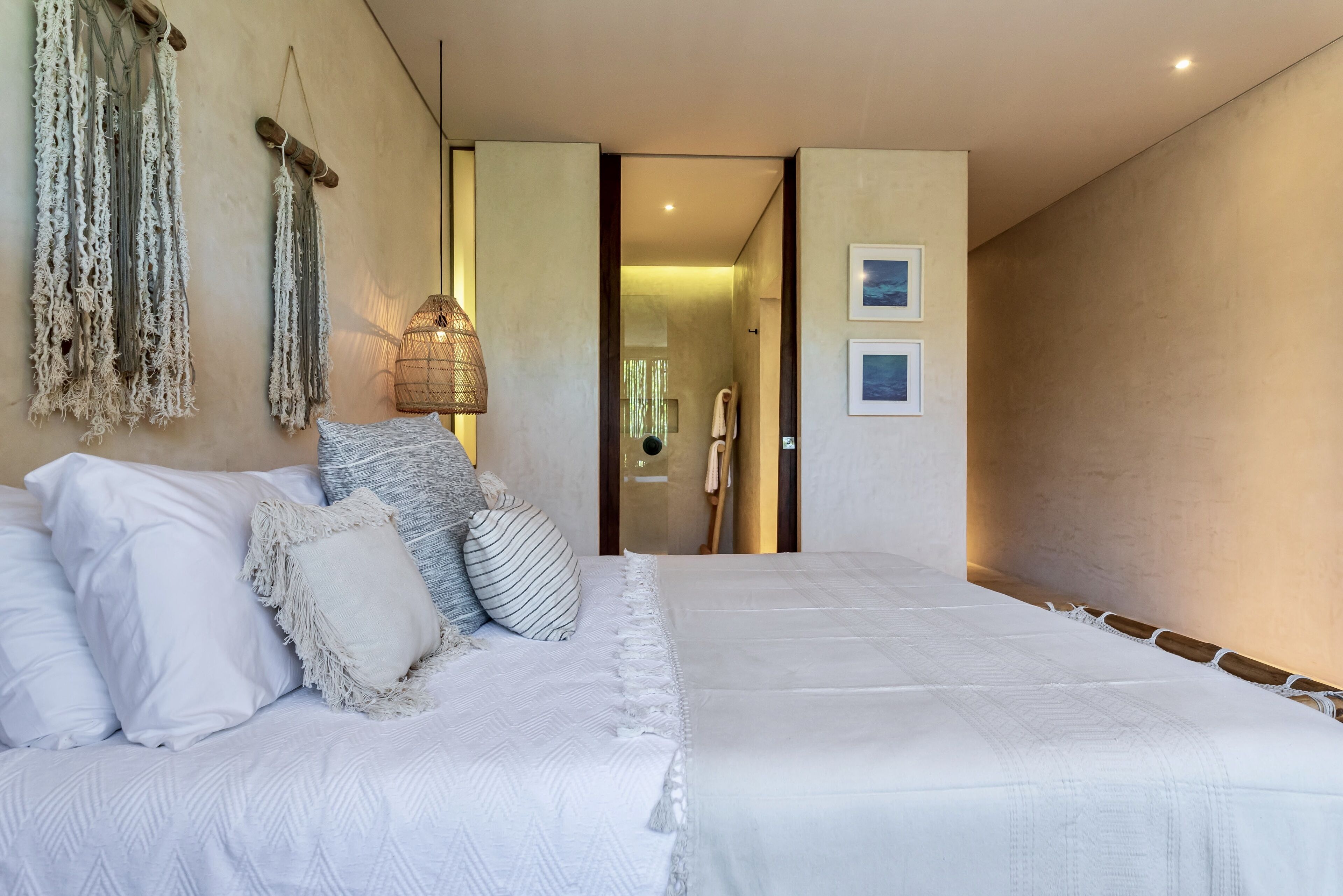 A bedroom with a large bed, a hanging macrame wall decoration, and a woven light fixture.