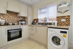 A compact kitchen with a built-in oven, a washing machine, and a window with blinds.