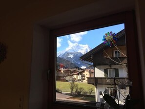 Une fenêtre donnant sur une montagne, une décoration colorée et un bâtiment doté d’un balcon.