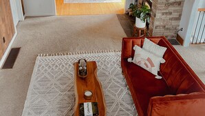 Un vaste espace de vie comprenant un canapé rouge, une table basse en bois et une cheminée. On aperçoit également un coin repas avec une table et des chaises en bois, visibles à travers une porte ouverte.