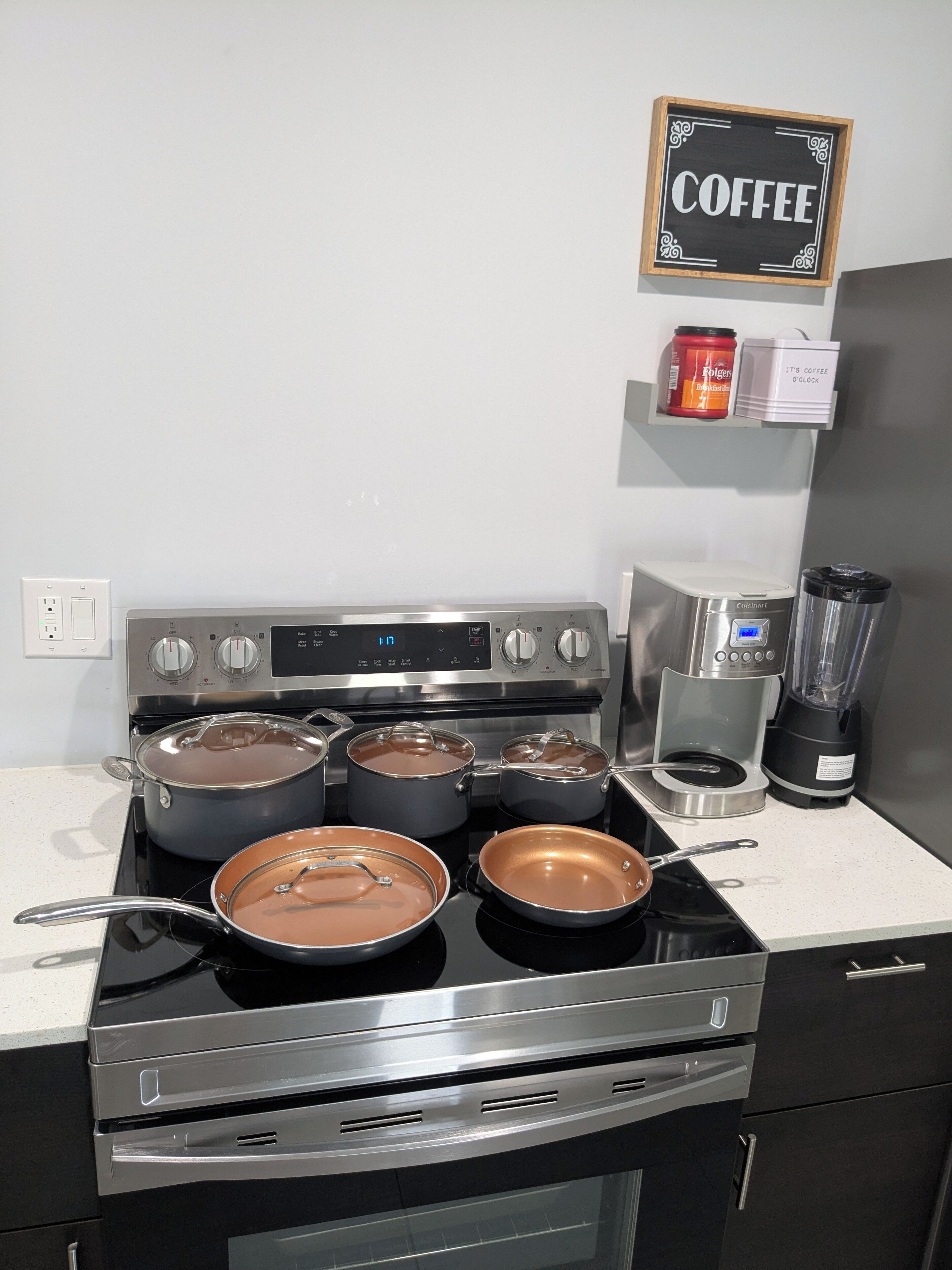 Una cocina con cuatro ollas en la estufa, una cafetera y una licuadora sobre el mostrador.