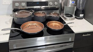 Una cucina con quattro pentole sul fornello, una macchina da caffè e un frullatore sul piano di lavoro.