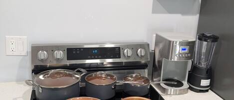 Una cocina con cuatro ollas en la estufa, una cafetera y una licuadora sobre el mostrador.